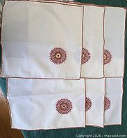 Six placemats laid out showing embroidered medallions and red stitched borders