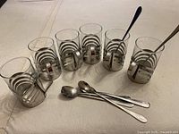 All six glasses in holders lined up with six teaspoons