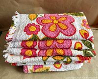 Stack of six folded white cotton terry towels showing multicoloured floral pattern and fringed edges