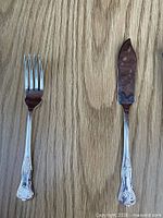 One fish fork and one fish knife on wood surface showing handle pattern and blade shape
