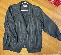 Front view of charcoal gray leather jacket showing collar, angled zipper, snaps, elastic hem