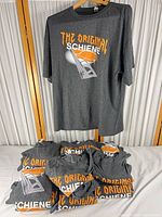 Front view of one T-shirt on hanger with additional folded shirts below