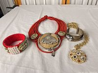 All four jewelry pieces laid out: red cuff, red statement necklace, silver cuff, gold pendant necklace