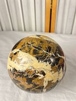 Overall view of polished stone sphere showing black, cream and brown veining