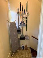 Overall lot showing ironing board, cleaning tools on wall rack and items on floor