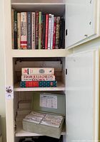 Cabinet shelf with row of cookbooks, two larger Julia Child volumes and recipe box below