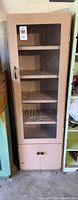 Full view of tall narrow beige metal cabinet with glass door, showing shelves and lower compartment