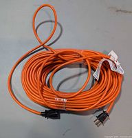 Entire coiled orange extension cord with both plug ends visible