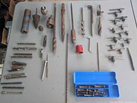 overview of approximately 50 mixed drill bits, hole saws, countersink cone, taps, chuck keys on tabletop