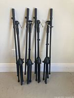 Four black microphone stands leaned against wall, full view