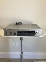 Front view of Akai AM-U310 amplifier on stand, power cord coiled on top