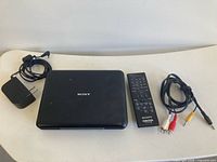 Portable DVD player, power adapter, remote, AV cable displayed on table