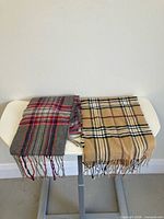 Two plaid scarves laid flat, grey and camel patterns visible with fringe