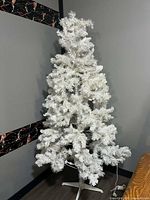 Full view of white artificial Christmas tree with stand and lights