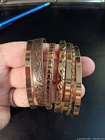 Six assorted patterned gold-tone bangles on hand