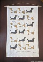 Front view of entire fabric wall hanging showing dachshund illustrations, text, dowel and hanger