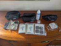 Full lot view showing two pulse massager units, electrode pads, carrying pouches, gel bottle, battery pack