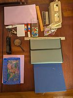 All items laid out on table showing folders, rulers, hole punch, stapler, magnifying glass, glue sticks, rubber bands, push pins, paper clips, binder clips