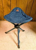 Full view of folded-out tripod stool showing legs, seat, carry strap