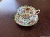 Teacup on saucer showing pattern, gilt trim and scalloped edges