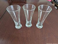 Three clear flared glasses side by side on table showing overall shape and condition
