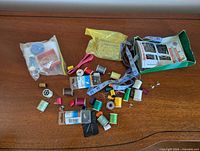 All sewing and craft supplies spread on surface showing thread spools, measuring tape, needle packs, nails box, ribbon, bobbin