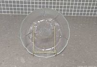 Front view of clear glass Arcoroc Fleur plate on stand showing full embossed pattern