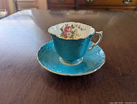 Teacup on saucer showing exterior teal color and gold trim