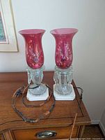 Front view of both cranberry glass lamps on marble bases with cords visible