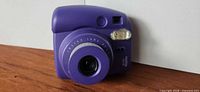 Front view of purple Fujifilm Instax Mini 8 camera showing lens, flash and branding