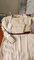 Front view of beige Béis sports duffle-backpack with detachable shoulder strap and laundry bag in foreground, tags attached