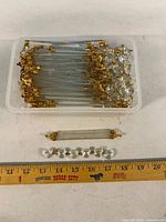 Container holding numerous clear glass twisted rod prisms with clips, single rod and octagon strand shown with ruler for scale