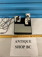 Front view of dual racing pedals with cable and ruler for scale