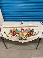 Full tree skirt laid flat showing entire embroidered design and red edge binding, yardstick for scale