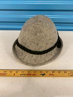 Full view of grey wool felt hat with braided green band, ruler for scale