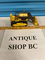 Full side view of yellow metal bulldozer toy next to ruler showing length ~8 in