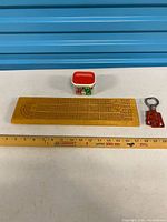 Full lot laid out: cribbage board, dice jar, bottle opener with measuring tape for scale