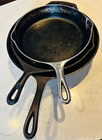 Three nested cast iron pans displaying handles and interiors