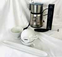 All items together: Breville frother, Zulay frother with box, two stacked and one single latte cups, ceramic filter cone, olive tray