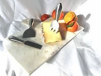 Board with cheese tools and oranges on cloth backdrop