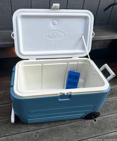Cooler open showing divided interior and ice pack, wheels visible