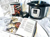 Instant Pot base with open inner pot, lid, digital device, trivet, two cookbooks