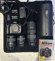 All items laid out: camera body, three lenses, batteries, charger, cable, strap, lens case, guidebook
