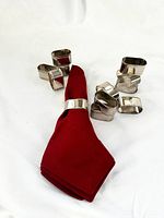 Group of silver napkin rings with red napkin displaying size and shape variety