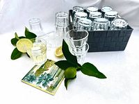 Glasses stacked upright and inverted in black woven basket; lemons and napkin props visible