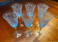 Six blue etched Fostoria goblets on wooden surface