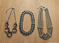 All three silver-tone necklaces side by side on wood surface