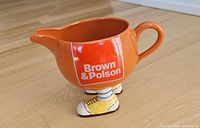 Full view left side of orange Carlton Ware Brown & Polson Walking Ware jug standing on shoe feet