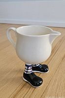 Front left view of ceramic creamer showing body, handle and legs with black boots