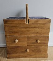 Front view of wooden sewing box showing drawers and handle